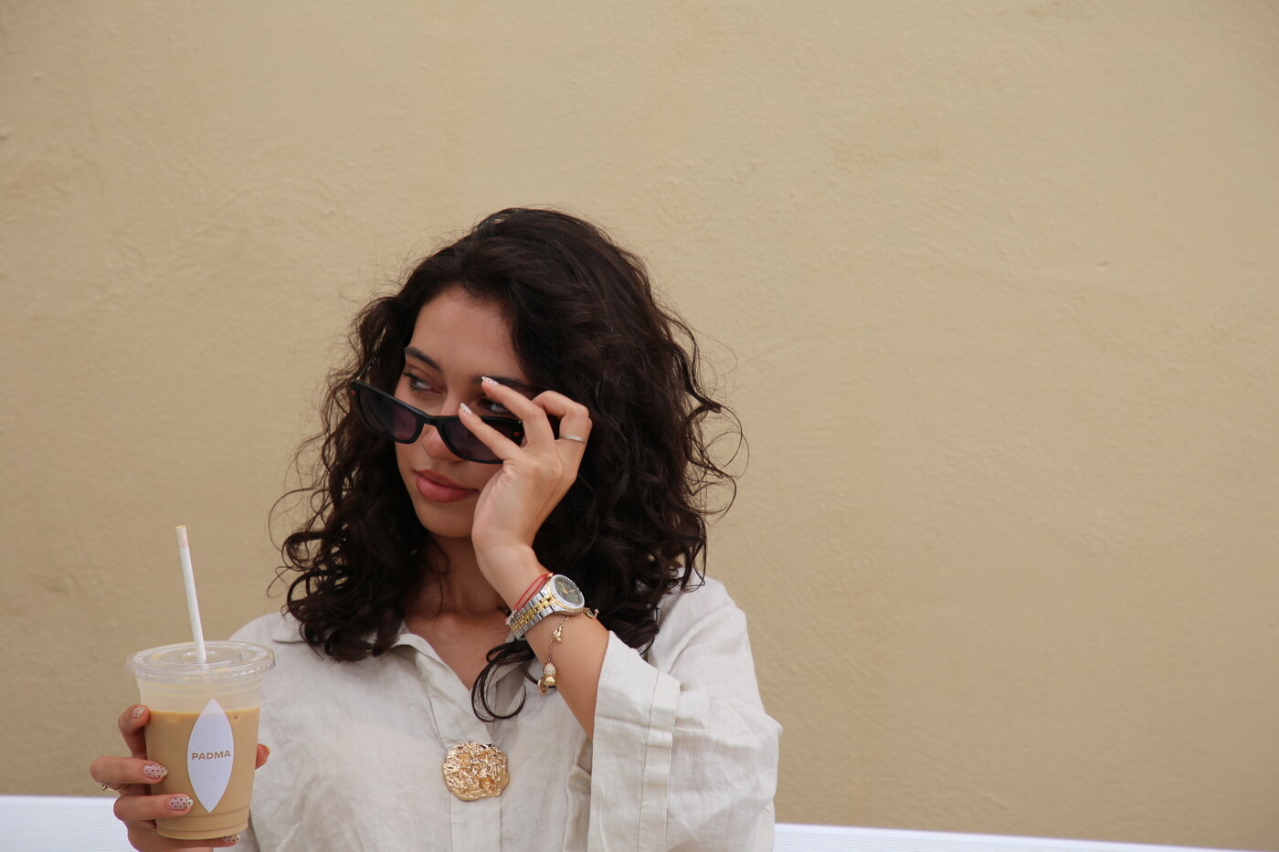 Portret cu un iced coffee PADMA și ochelari de soare, pe fundal crem
